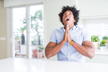 African American business man begging and praying with hands together with hope expression on face very emotional and worried. Asking for forgiveness. Religion concept.