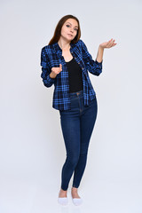 Full-length Vertical Portrait of a cute brunette girl, a young woman with beautiful curly hair in a blue shirt and jeans on a white background. Smiling, talking with emotions, showing hands.