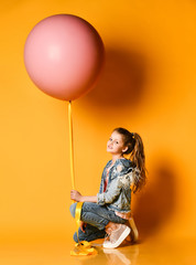 Fototapeta na wymiar Young beautiful teenager girl posing on a yellow background, lies and holds up a huge giant pink balloon. Summer style.