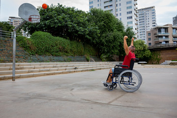 Cripple man in wheelchair plays basketball on open air ground