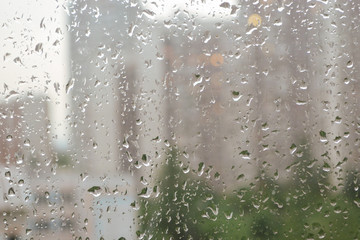 Drops of rain water on a window glass. Cityscape in defocus outside the window. Cloudy weather, sadness.