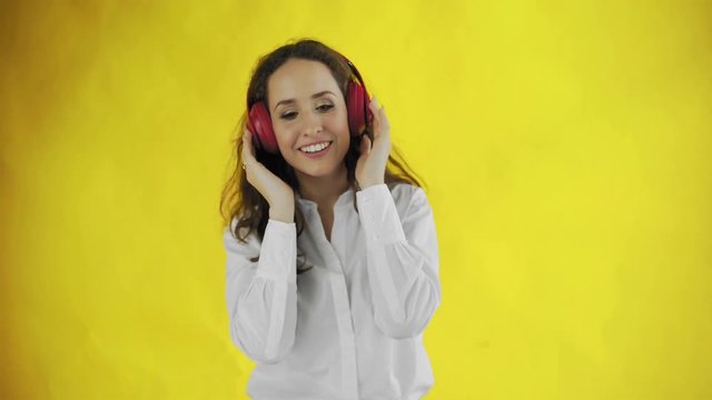 Woman listening to music with red headphones in Studio with yellow Background.
