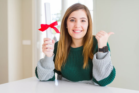 Beautiful young woman holding degree with red bow pointing and showing with thumb up to the side with happy face smiling