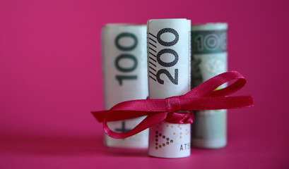 Polish national currency zloty banknotes of 200 and 100 rolled and tied with red ribbon looks like gift / present, close up, isolated on pink / purple background