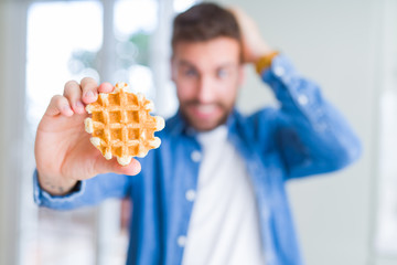 Handsome man eating sweet Belgian pancakes stressed with hand on head, shocked with shame and surprise face, angry and frustrated. Fear and upset for mistake.