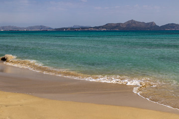 Scenic view at beach of Port de Pollenca on balearic island Mallorca, Spain on a sunny day with clear blue water, sand mountain range and houses in background