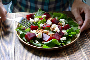 Woman eating warm autumn beetroot salad with soft cheese, walnuts and spinach in a plate on a wooden background
