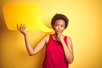 Young african american woman holding speech bubble over yellow isolated background serious face...