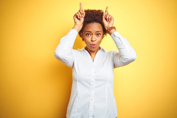 African american business woman over isolated yellow background doing funny gesture with finger over head as bull horns