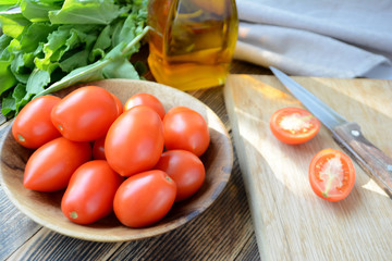 Fresh ripe organic tomatoes in a wooden bowl. Ingredients for summer salad: tomatoes, spinach, olive oil
