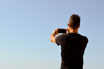 Man wearing black t-shirt photographing the landscape with his cell phone