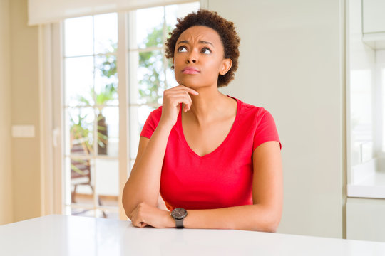 Young beautiful african american woman at home with hand on chin thinking about question, pensive expression. Smiling with thoughtful face. Doubt concept.