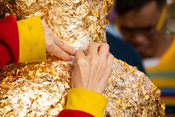 Close-up of woman hand making merit. Gilding gold leaf onto the Buddha statue image.