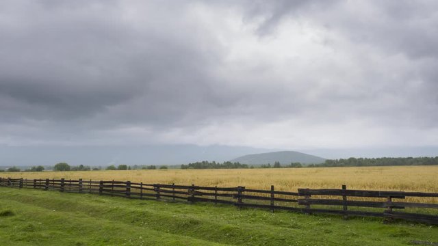 Timelapse. Autumn landscape of a valley with green grass in front of high mountains in cloudy weather with moving clouds on a gray sky