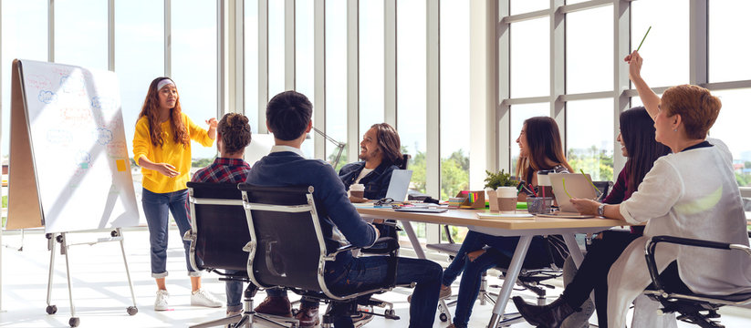 Young Asian Creative Hipster Female Leader Standing And Making Presentation At Modern Office Happy Talking And Brainstorming Idea With Teamwork. Casual Asian People Business Meeting Workshop Concept.