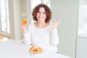 Senior woman eating sweet belgian waffle very happy pointing with hand and finger to the side