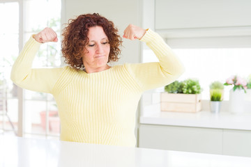 Beautiful senior woman wearing yellow sweater showing arms muscles smiling proud. Fitness concept.