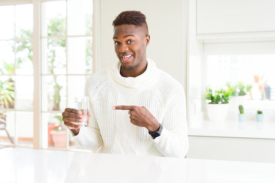 African american man driking a fresh glass of water very happy pointing with hand and finger