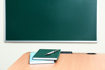 Wooden school desk with stationery near chalkboard in classroom