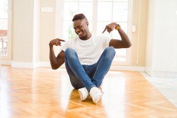 Handsome african american man sitting on the floor at home looking confident with smile on face, pointing oneself with fingers proud and happy.
