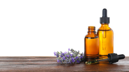 Bottles of essential oil and lavender flowers on wooden table against white background