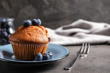 Plate with tasty muffin and blueberries on grey table. Space for text
