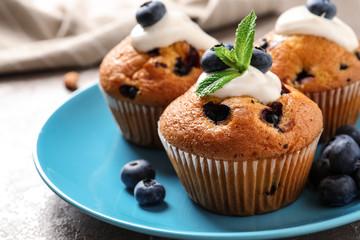 Plate of tasty muffins and blueberries on marble table, closeup