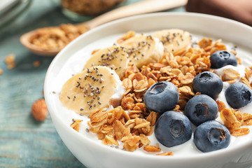 Bowl of yogurt with blueberries, banana and oatmeal on wooden table, closeup