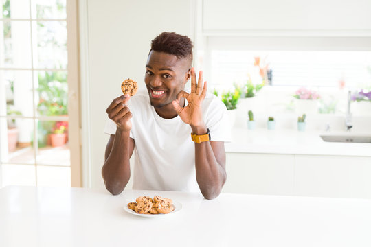 Young African American Man Eating Chocolate Chips Cookies Doing Ok Sign With Fingers, Excellent Symbol