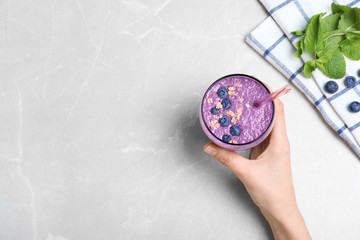 Woman holding glass of delicious blueberry smoothie on light marble table, top view. Space for text