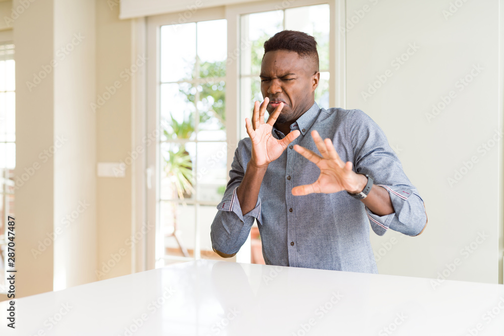 Canvas Prints Handsome african american man on white table disgusted expression, displeased and fearful doing disgust face because aversion reaction. With hands raised. Annoying concept.