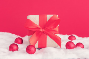 Christmas toys and gift with red ribbon, white snow made of cotton, red background, copy space. Winter holidays concept