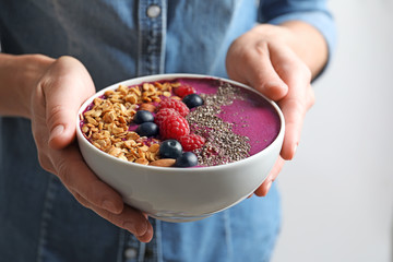 Woman holding bowl of acai smoothie with granola and berries, closeup
