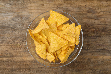 Glass bowl with tasty Mexican nachos chips on wooden table, top view