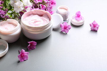 Jars of body cream and flowers on grey background. Space for text
