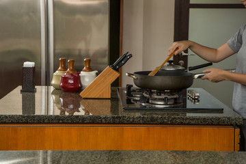 Woman standing in the kitchen and preparing food in a small saucepan on the gas stove