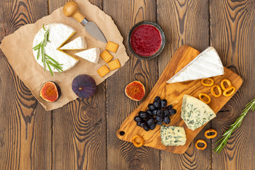 Cheese plate served with jam, figs, crackers and herbs on a wooden background. Place under the text. Flat lay.