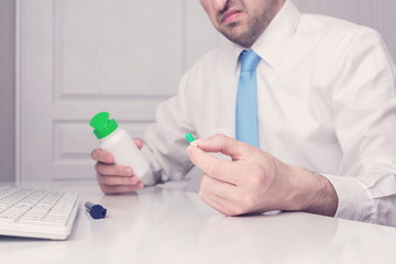 Fototapeta premium Man working in the office, doesn't want to take his medicine, close up, toned