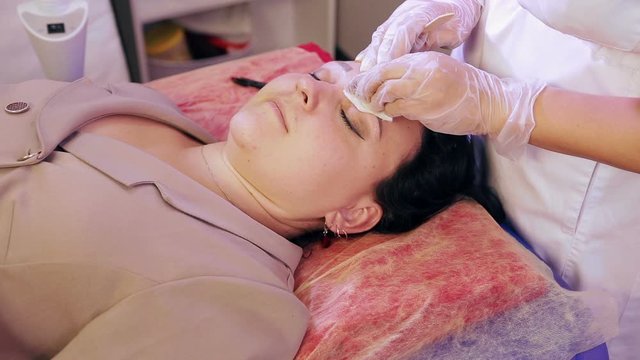 The beautician wipes the client's face with a disinfectant solution before depilation.