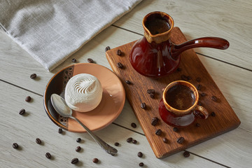 cup of coffee with cezve and marshmallow on a wooden table