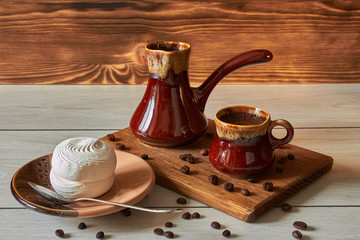 cup of coffee with cezve and marshmallow on a wooden table