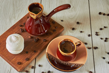 cup of coffee with cezve and marshmallow on a wooden table