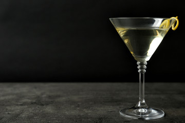 Glass of lemon drop martini cocktail with zest on stone table against black background. Space for text