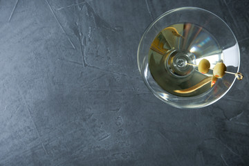 Glass of Classic Dry Martini with olives on dark grey table, top view. Space for text