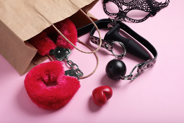Paper shopping bag with different sex toys on pink background