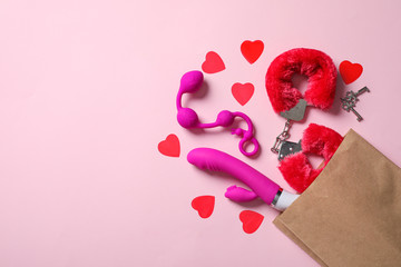 Paper shopping bag with different sex toys on pink background, flat lay. Space for text