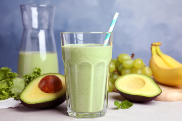 Glass of tasty smoothie and avocado on light grey table