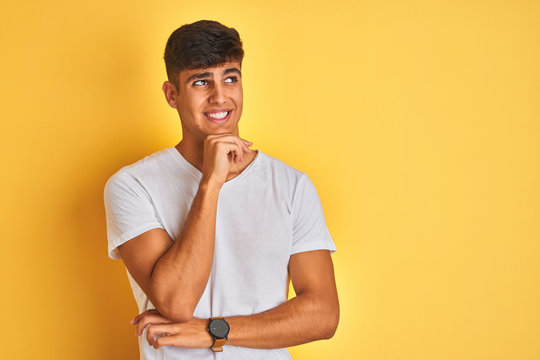 Young indian man wearing white t-shirt standing over isolated yellow background Thinking worried about a question, concerned and nervous with hand on chin