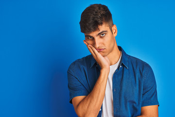 Young indian man wearing shirt standing over isolated blue background thinking looking tired and bored with depression problems with crossed arms.