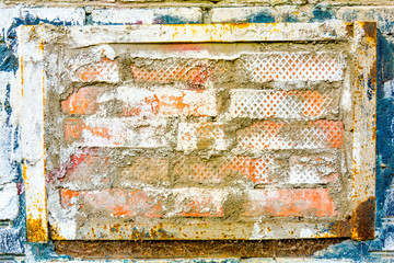 On old brick wall is insert of other bricks in rusty metal frame, peeling paint